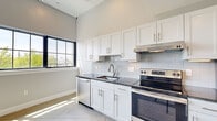 Located at 1 Upper Falls Rd in Biddeford, Maine, this thoughtfully designed single-floor unit blends modern finishes with an industrial aesthetic. The open layout makes efficient use of the space, highlighted by polished concrete floors and soaring ceilings that lend an airy, loft-like feel throughout.

The kitchen is a standout feature, outfitted with white shaker-style cabinetry, dark granite countertops, a classic subway tile backsplash, and a full suite of stainless steel appliances — including a dishwasher, electric range, and refrigerator. A single-basin sink with a brushed gold faucet adds a refined touch, while recessed under-cabinet lighting enhances both function and ambiance.

The main living area is bathed in natural light, courtesy of large, multi-pane black-framed windows that frame views of the surrounding Biddeford streetscape and greenery. Roller shades provide privacy and light control. A wall-mounted HVAC unit and baseboard heating ensure year-round comfort.

The bathroom is clean and functional, featuring a white shaker vanity with a gold-toned faucet, a large mirror with overhead lighting, and a walk-in shower with a white surround. The space maintains the unit's consistent modern palette of whites and neutrals throughout.