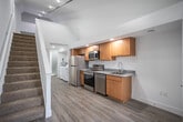 Located at 5737 E Town Dr in Hudsonville, Michigan, this three-floor residence offers a thoughtfully designed layout with functional spaces spread across each level. The main floor showcases a fully equipped kitchen featuring warm-toned wood cabinetry, granite countertops, and a complete suite of stainless steel appliances including a refrigerator, electric range, built-in microwave, and dishwasher. Durable wood-look flooring runs throughout the main level, complemented by recessed and track lighting that brightens the open space. A staircase with clean white railings connects the floors seamlessly. The bathroom is finished with matching granite countertops, a wood vanity, and a tub-shower combination. Upper floor areas feature plush carpeting and sloped ceilings that add architectural character, with a window providing natural light. A dedicated utility area houses a full-size washer and dryer alongside a water heater, offering added convenience. The lower level provides additional carpeted flex space, complete with an electrical panel and recessed lighting. Throughout all three floors, crisp white walls and clean finishes create a bright, move-in-ready atmosphere well-suited for comfortable everyday living.