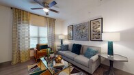 This thoughtfully designed one-bedroom, one-bathroom model unit offers a cohesive and modern living experience across a single floor. The living area serves as the heart of the unit, featuring wood-style flooring, a ceiling fan, and natural light streaming through large windows dressed with patterned drapes and blinds. A gallery wall of framed artwork lends a polished, curated character to the space, which is anchored by a glass-topped coffee table and comfortable seating.

The galley-style kitchen is well-equipped, showcasing rich dark-espresso cabinetry, granite countertops, a full suite of black appliances including an electric range, microwave, refrigerator, and dishwasher, along with a tiled backsplash and light wood-style flooring that keeps the space feeling bright and clean.

The bedroom offers plush carpeting, a ceiling fan, ample natural light from a window with coordinating drapes, and generous space for furniture and storage. The room's warm, restful ambiance is further enhanced by thoughtful design details.

The bathroom features granite-topped dark cabinetry that mirrors the kitchen's aesthetic, a tub-shower combination, and wood-style flooring, completing the unit's consistent and refined design language throughout.