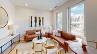 This thoughtfully designed single-floor residence blends contemporary architecture with mid-century modern aesthetics to create a warm and inviting living environment. Light hardwood flooring flows throughout the main living spaces, lending a sense of continuity and warmth.

The living room is a standout area, featuring large floor-to-ceiling windows that frame outdoor views of a tree-lined neighborhood, flooding the space with abundant natural light. Rich cognac leather sofas, a woven area rug, and curated wall art lend the room a sophisticated yet comfortable character.

The kitchen is efficiently laid out and well-appointed, featuring white upper cabinetry paired with warm wood-toned lower cabinets and stainless steel appliances, including a range, microwave, and refrigerator. A subway tile backsplash adds a clean, classic touch, while a large window brings in ample daylight and neighborhood views, making the space feel open and airy. A compact dining area adjacent to the kitchen offers a charming spot for everyday meals.

The bedroom is serene and understated, with soft neutral tones, light hardwood floors, and a built-in closet providing practical storage. A hallway connects the spaces seamlessly, adorned with colorful framed artwork that adds personality throughout.

The bathroom is clean and modern, featuring a floating wood-grain vanity with a white countertop, a large mirror, tile flooring, and a tub-shower combination with tile surround — all finished to a high standard.