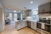 Located at 119 W Court St in Ithaca, NY, this thoughtfully designed two-bedroom, one-bathroom unit offers a clean, modern aesthetic across its single-floor layout. The open-concept kitchen serves as a central feature, showcasing gray shaker-style cabinetry, white quartz countertops, stainless steel appliances including a French door refrigerator and dishwasher, and a peninsula with bar seating for two — ideal for casual dining or working from home. Track lighting and recessed fixtures illuminate the space effectively. Light hardwood flooring flows through the kitchen and living areas, adding warmth to the neutral color palette.

The living area benefits from multiple large windows framing street-level views of the surrounding Ithaca neighborhood, filling the space with natural light. Crown molding adds a refined architectural detail to this room.

The primary bedroom is comfortably sized, featuring plush carpet, dual windows with roller shades, and a double-door closet. The second bedroom offers similar finishes and natural light. The full bathroom is notably spacious, finished with large-format tile flooring, a white subway tile walk-in shower with grab bars, a recessed vanity, and a backlit mirror — combining accessibility with contemporary style.