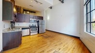 Located in a historic downtown Winston-Salem building, this one-bedroom, one-bathroom unit offers an urban loft aesthetic with distinctive industrial charm. The open living and kitchen area features warm hardwood floors, soaring ceilings with exposed ductwork, and track lighting. The kitchen is equipped with stainless steel appliances, granite countertops, dark wood cabinetry, and a built-in wine rack. The bedroom includes a spacious walk-in closet with built-in shelving. The bathroom offers a clean, tiled design with a full tub-shower combination. A hallway connects the spaces, completing this efficiently designed urban residence.