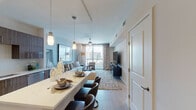 This single-floor residence offers a thoughtfully designed open-concept layout with contemporary finishes and sweeping urban skyline views. The living area serves as the heart of the space, featuring a ceiling fan, large floor-to-ceiling windows that flood the room with natural light, and direct views of the surrounding cityscape. Neutral tones and modern décor create a calm, sophisticated ambiance throughout.

The kitchen is well-equipped with wood-grain flat-front cabinetry extending to the ceiling, stainless steel appliances including a French door refrigerator, gas range, built-in microwave, and dishwasher. A white quartz waterfall island with seating provides both workspace and a casual dining area, complemented by pendant lighting overhead. Track lighting illuminates the full length of the kitchen.

Two bedrooms each offer ceiling fans and large windows with city views, providing ample natural light and an elevated sense of openness. Neutral wall tones and clean lines maintain the modern aesthetic.

The bathroom features a double-sink vanity with a wood-toned base, white quartz countertops, a large framed mirror, and a shower-tub combination. Light tile flooring and clean white walls keep the space bright and functional. The overall design balances urban sophistication with livable comfort.