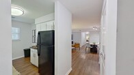 Unit F62 at 200 Westminster Drive in Chapel Hill, NC is a well-appointed 1-bedroom, 2-bathroom apartment spanning 920 square feet on a single floor. The open-concept living and dining area is anchored by warm hardwood-style flooring throughout, large windows that invite abundant natural light, and a clean, neutral color palette that lends a bright and airy feel to the space. The living room offers generous proportions with a wide window framed by curtains, creating a comfortable and inviting atmosphere. Adjacent to it, the dining area accommodates a round table for four and features track lighting overhead. The galley-style kitchen is outfitted with white shaker cabinetry, dark granite countertops, a subway tile backsplash, stainless steel sink, and black appliances including a refrigerator, range, and microwave. The primary bedroom measures 180 square feet and features plush carpeting, a window with natural light, and access to two closets. Both bathrooms are finished with white vanities featuring granite countertops and brushed nickel hardware; one includes a shower-tub combo. The unit also benefits from two closets for ample storage throughout.