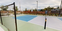 This residential development on Nutmeg St in Murrieta, CA, showcases a blend of modern architecture and recreational facilities. The centerpiece is a set of pristine tennis courts, featuring vibrant blue and green surfaces that contrast beautifully with the surrounding landscape. The courts are equipped with regulation nets and are illuminated by strategically placed lighting fixtures for evening play.

The complex boasts multi-story apartment buildings with a contemporary design, featuring earth-toned exteriors and balconies. Surrounding the tennis courts are meticulously landscaped areas with young trees, shrubs, and drought-resistant plants, adhering to the local climate. A brick perimeter wall provides privacy and security for residents.

The community layout promotes an active lifestyle, with paved walkways connecting the residential buildings to the recreational areas. Additional amenities visible include covered parking structures and open green spaces. The overall design creates an inviting atmosphere that balances urban living with outdoor recreation, making it an attractive option for those seeking a modern, amenity-rich residential experience in Southern California.