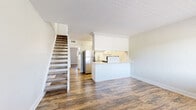 This two-story, two-bedroom, two-bathroom home is thoughtfully laid out across two floors, offering a practical and efficient use of space. The main level features an open-concept kitchen and living area with warm wood-look flooring that runs throughout the home. The kitchen is equipped with white cabinetry, stainless steel appliances including a full-size refrigerator, and a peninsula that separates it from the living area, providing additional counter space and a natural division of the room. A staircase with carpeted treads connects the main level to the upper floor. Both bathrooms are finished with white vanities and full tub-shower combinations featuring large-format marble-style tile surrounds with chrome fixtures. A dedicated laundry room houses a stacked washer and dryer unit, adding everyday convenience. The primary bedroom is generously sized, featuring tall ceilings, a ceiling fan, and access to an adjoining hallway leading to the laundry and bathroom. The secondary bedroom benefits from natural light through a window with outdoor views. Neutral walls, white trim, and textured ceilings are consistent throughout, creating a clean and cohesive aesthetic across the entire home.