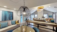 The clubhouse at 3675 Barnard in Oceanside is a thoughtfully designed single-story community space that blends contemporary aesthetics with comfortable functionality. The interior is characterized by vaulted ceilings that lend an open, airy quality to the room, while recessed lighting and an array of distinctive pendant fixtures — including a striking oversized wire cage chandelier and a tiered drum shade light — create a warm, layered ambiance throughout.

The main gathering area features light hardwood-style flooring that complements the neutral wall tones and modern furnishings. A full-size shuffleboard table serves as a central recreational focal point, making the space well-suited for social events and casual entertainment. A comfortable lounge seating area with a tufted sofa, teal accent chairs, and gold side tables adds a relaxed, stylish corner for residents to unwind.

Decorative elements, including framed artwork, curated accessories, and a candle lantern centerpiece on the round dining table, contribute to the clubhouse's polished yet approachable character. Natural light filters in through multiple windows and a glass door, connecting the interior to the outdoor surroundings.
