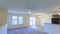 This two-floor space features a welcoming, open-concept living area that serves as the heart of the home. The main living space is finished with plush carpet and benefits from abundant natural light, courtesy of a large multi-pane window and a sliding glass door that opens to an outdoor balcony, offering views of the surrounding neighborhood. The sliding door provides a seamless connection between the interior and exterior, enhancing the sense of openness throughout.

Overhead, a ceiling fan with an integrated light fixture ensures comfortable airflow, while an elegant chandelier nearby adds a refined touch to the dining or transitional area. The neutral, light-toned walls and standard-height ceilings contribute to a clean, versatile aesthetic that adapts easily to various interior styles.

A partial wall or counter is visible along one edge of the living area, suggesting an adjacent kitchen space with a convenient pass-through or breakfast bar layout. Recessed vents are integrated into the ceiling, indicating a central HVAC system throughout.

Overall, the space presents a functional, well-lit layout with a balance of comfort and practicality across its two floors.