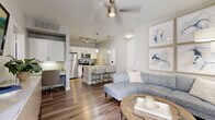 Located at 14200 Vance Jackson Road in San Antonio, TX, this well-appointed one-bedroom, one-bathroom unit offers a thoughtfully designed open-concept layout across a single floor. Rich hardwood-style flooring flows throughout the main living areas, anchoring the bright and airy aesthetic defined by neutral gray walls and abundant natural light from large windows dressed with sheer curtains and blinds.

The living room is inviting and functional, featuring a ceiling fan, wall-mounted TV, and direct access to a private patio. It connects seamlessly to the kitchen, which is equipped with stainless steel appliances — including a refrigerator, range, microwave, and dishwasher — white cabinetry, granite-style countertops, pendant lighting, and a breakfast bar with seating. A dedicated nook provides additional workspace or study space.

The bedroom is carpeted for comfort, includes a ceiling fan, and benefits from a sliding glass door that lets in natural light. A full bathroom offers a granite-topped vanity with white cabinetry, a tiled tub-shower combination, and hardwood-style flooring. The unit is completed by an in-unit laundry area, a closet, and a hallway connecting all spaces efficiently.