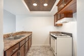 Located at 610 N Garfield St in Santa Ana, CA, this two-story, three-bedroom, one-bathroom residence offers a practical and comfortable layout across two generously sized floors. The main level provides the majority of the living space, while the upper level offers additional square footage for flexible use.

The kitchen is a functional highlight of the home, featuring rich dark wood cabinetry, stone-toned countertops, a double-basin sink, and a gas range. A distinctive tray ceiling with wood paneling and recessed lighting adds a warm architectural touch overhead. The kitchen opens toward the living area through a peninsula counter, creating an open and connected feel.

Each of the three bedrooms is carpeted and finished with neutral gray walls, offering a calm and move-in-ready aesthetic. Closets with built-in rods provide practical storage. One bedroom features a sliding glass door with vertical blinds that leads directly to a private balcony, where panoramic views of the surrounding Santa Ana neighborhood unfold under the Southern California sky — with palm trees, rooftops, and open blue skies visible in the distance.

The bathroom is clean and simply appointed with tile flooring, a white vanity, and a towel bar. Tile flooring also runs through the kitchen and entryway areas, complementing the polished look of the main living spaces. Natural light filters through windows throughout the unit, keeping the interiors bright and inviting.