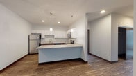 This well-appointed single-floor unit offers a thoughtfully designed open-concept layout that seamlessly connects the kitchen and living areas. The kitchen is a standout feature, showcasing crisp white upper cabinetry paired with rich dark lower cabinets, granite-inspired countertops, and a full suite of stainless steel appliances including a refrigerator, electric range, microwave, and dishwasher. A peninsula with a matching stone countertop extends the kitchen workspace and serves as a natural divider between the cooking and living areas. Pendant lighting adds a refined touch overhead, while recessed lighting ensures the space is well lit throughout. Durable hardwood-style flooring runs through the main living areas, providing both visual warmth and easy maintenance. The living area benefits from a large sliding glass door fitted with vertical blinds, inviting natural light and offering outdoor access. Two carpeted bedrooms provide comfortable retreats; the primary bedroom features large windows with neighborhood views and a generous closet. The unit includes two bathrooms, each finished with dark wood vanities, white countertops, large mirrors, and light-toned flooring. One bathroom includes a walk-in shower, while the other offers additional square footage for accessible use. Dark baseboards throughout create a cohesive, modern aesthetic.