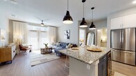 This single-floor residence offers a thoughtfully designed open-concept layout that seamlessly connects the kitchen, dining, and living areas. The kitchen is a standout feature, equipped with stainless steel appliances, crisp white shaker cabinetry, a white subway tile backsplash, and granite countertops extending across a central island with bar seating beneath three industrial-style pendant lights. Wood-look flooring runs throughout the main living areas, adding warmth and continuity to the space.

The living room benefits from generous natural light streaming through floor-to-ceiling French doors dressed with sheer white curtains and horizontal blinds. A ceiling fan overhead enhances comfort in this bright, airy space. The open floor plan creates a smooth transition between entertaining and relaxing areas.

Both bedrooms are carpeted and receive ample natural light through large windows with blinds and sheer curtains. The primary bedroom includes an en-suite bathroom featuring a glass-enclosed shower, granite vanity countertops, white cabinetry, and direct access to a walk-in closet. A second bathroom offers a full tub-shower combination with clean tile surround. The overall aesthetic throughout is contemporary and cohesive, characterized by neutral tones and modern finishes.