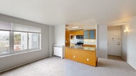 This single-floor residence features a thoughtfully designed open-concept layout that seamlessly connects the living area and kitchen. The spacious living room is finished with plush wall-to-wall carpeting and neutral gray walls, creating a calm, versatile backdrop. A wide picture window along the exterior wall frames expansive city and neighborhood views, while baseboard heating units ensure year-round comfort.

The kitchen is efficiently designed with warm honey-toned wood cabinetry, granite countertops, and a full suite of stainless steel appliances including a gas range, dishwasher, and built-in microwave. Light tile flooring and a window above the sink bring natural light into the cooking space. A peninsula with matching granite and storage drawers below connects the kitchen to the living area, functioning well as a casual dining or prep surface.

The bedrooms are generously proportioned, each carpeted and featuring sliding closet doors and windows with neighborhood views. The full bathroom is finished with classic white subway tile surrounding the tub-shower combination, a pedestal sink, chrome fixtures, and light tile flooring, maintaining a clean, timeless aesthetic throughout.