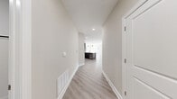 This thoughtfully designed single-floor residence offers a clean, contemporary aesthetic throughout, highlighted by light-toned luxury vinyl plank flooring, recessed lighting, and neutral wall tones that create a bright, welcoming atmosphere. A wide hallway with crisp white trim and baseboards leads into an open-concept living and kitchen area, where large windows flood the space with natural light and provide outdoor views.

The kitchen is a standout feature, boasting dark charcoal flat-panel cabinetry, white quartz countertops, a tile backsplash, and a full suite of stainless steel appliances including a gas range, built-in microwave, and French door refrigerator. A central island with a sink adds both functionality and visual interest.

The living area is anchored by a sleek gas fireplace and a generous bank of windows overlooking the surrounding landscape. Sliding glass doors open directly onto a private balcony, extending the living space outdoors.

The bedroom features plush wall-to-wall carpeting, recessed lighting, and access to a well-organized walk-in closet with built-in shelving and hanging rods. An additional room with hardwood-style flooring and a large window offers flexibility as a bedroom, office, or den. The bathroom is finished with large-format white tile, a decorative mosaic accent border, and a soaking tub with brushed nickel fixtures.