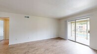 This single-floor, 2-bedroom, 1-bathroom unit offers a functional and well-organized layout designed for comfortable everyday living. The open living room is a bright, welcoming space featuring light wood-look flooring, crisp white walls, and a sliding glass door that fills the area with natural light and provides direct access to an outdoor patio. The living area flows into the kitchen via a convenient pass-through counter with a granite-style surface, offering an open connection between the two spaces. The kitchen is equipped with warm wood cabinetry, a granite countertop, and black appliances, including a full-size refrigerator. A hallway connects the main living areas to the private quarters of the home. Both bedrooms are finished with plush, neutral-toned carpet and bright white walls, creating a calm and restful atmosphere. The primary bedroom is a generously sized room, while the secondary bedroom features a window that lets in natural light and views of the surrounding area. Both bedrooms are outfitted with built-in closets featuring bi-fold doors, providing ample storage. The shared bathroom includes a full tub and shower combo with warm earth-toned tile surround, a wood vanity with granite countertop, and wood-look flooring, completing the unit's cohesive and clean aesthetic.