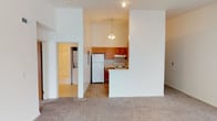This single-story space offers a functional and straightforward layout designed for comfortable everyday living. The living area is generously sized, featuring neutral wall-to-wall carpeting and large sliding glass doors fitted with vertical blinds that allow natural light to fill the room. A dedicated entry area provides a clear separation from the main living space.

The kitchen is positioned adjacent to the living area, separated by a half-wall peninsula that creates an open feel while defining the cooking zone. Warm-toned oak cabinetry lines the walls, providing ample storage, while white appliances — including a full-size refrigerator and electric coil range with overhead ventilation — offer essential functionality. A pendant chandelier above the kitchen adds a touch of warmth to the space. Tile-style flooring runs through the kitchen, transitioning to carpet in the adjoining areas.

The bedroom is a well-proportioned room with carpet flooring, a ceiling fan with light fixture, and a window with blinds for natural light and privacy. Doorways connect to additional spaces, including a closet area. The bathroom includes a single-sink vanity with wood cabinetry, a large mirror with overhead lighting, and a full tub and shower combination with a sliding glass enclosure.