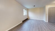 This 490 square foot apartment in Albion, NY offers a thoughtful single-floor layout with one bedroom and one bathroom. The living area is characterized by its modern aesthetic, featuring sleek gray laminate flooring throughout and cream-colored walls that create a bright, airy atmosphere. Large windows in both the living room and bedroom allow for plenty of natural light, enhancing the sense of space.

The living room is generously sized, providing ample space for both seating and dining areas. A notable feature is the baseboard heating system, ensuring comfort during colder months. The bedroom, measuring 140 square feet, offers sufficient space for a queen-sized bed and additional furniture.

The bathroom, while compact, is efficiently designed with a modern toilet and likely includes a shower (though not visible in the provided images). The apartment's interior doors are a classic paneled style in a light gray color, adding a touch of traditional charm to the otherwise contemporary space.

Storage appears to be addressed through closet space, as evidenced by the double bi-fold doors visible in one of the images. The kitchen, while not shown, is likely integrated into the open plan living area, maintaining the apartment's flow and functionality.

Overall, this apartment presents a fresh, updated living space ideal for single occupants or couples seeking a low-maintenance, modern home in a small town setting.