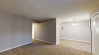 Located at 3011 S Leonard Springs Rd in Bloomington, Indiana, this two-bedroom, one-bathroom residence offers a straightforward and functional single-floor layout. The living room features neutral-toned walls, soft carpeting, and a textured ceiling, creating a comfortable and understated atmosphere. It flows naturally into the dining area, which is accented by a classic chandelier and tile flooring, providing a clear distinction between living and dining spaces. The kitchen is efficiently arranged with white cabinetry, a countertop sink, a range, and a full-size refrigerator, all set atop durable tile flooring with ample cabinet storage overhead. The two bedrooms are carpeted and finished in warm neutral tones; the primary bedroom includes a wide louvered closet for generous storage, while the second bedroom benefits from a window that allows natural light and outdoor views. Three closets throughout the unit provide practical storage solutions. The bathroom is clean and functional, featuring a tub-shower combination, a vanity, and matching tile flooring consistent with the rest of the non-carpeted areas. A connecting hallway ties all rooms together, contributing to an efficient and cohesive floor plan throughout the home.