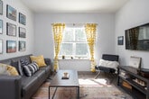 This single-floor residence offers a thoughtfully designed open-concept layout that seamlessly connects the kitchen and living areas. The kitchen is a standout feature, equipped with rich dark cabinetry, granite countertops, and a full suite of stainless steel appliances including a range, microwave, dishwasher, and refrigerator. A central island with a matching granite surface and bar seating serves as both a functional prep space and a casual dining spot, illuminated by stylish gold pendant lights overhead. Light wood-style flooring runs throughout the kitchen and living areas, adding warmth and continuity to the space. The living room is bright and inviting, benefiting from natural light through a large window dressed with patterned curtains. The bedroom offers plush carpeting, a window with natural light, and direct sightlines to the kitchen, creating a cohesive and connected feel. The bathroom is clean and functional, featuring a granite-topped dark vanity, a full soaking tub with shower, and tasteful decorative shelving. Throughout the residence, neutral wall tones provide a versatile backdrop, making the space feel open, airy, and move-in ready.
