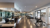 Located at 200 W Edge Way in Lynchburg, Virginia, this fitness center offers a comprehensive exercise space designed for an effective and comfortable workout experience. The single-floor facility is laid out in an open, elongated floor plan that maximizes usability and flow between equipment zones.

The room features polished concrete flooring throughout, lending a clean, modern industrial aesthetic that is both durable and easy to maintain. Floor-to-ceiling mirrors line multiple walls, visually expanding the space and allowing users to monitor their form during workouts. Recessed lighting provides bright, even illumination throughout the room.

Cardio equipment is well-represented, with a row of treadmills arranged along the central corridor and cycling bikes positioned throughout the space. An elliptical machine adds additional low-impact cardio options. The strength training area includes a dumbbell rack with a full range of free weights, medicine balls, and a weight bench, catering to a variety of resistance training needs.

Large sliding glass doors and expansive windows connect the interior to an adjacent communal area, allowing ample natural light to flow into the gym and providing views of the surrounding property. A wall-mounted split-system air conditioning unit ensures a comfortable climate year-round. The overall ambiance is modern, functional, and inviting, making this fitness center a practical and well-appointed amenity.