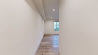 Located at 6104 Cahuenga Blvd in the North Hollywood neighborhood of Los Angeles, this two-story unit offers a clean, modern aesthetic across two well-proportioned floors. Light-toned wood flooring runs throughout, complementing the crisp white walls and recessed lighting that keep every area feeling bright and open.

The ground floor features a generously sized living area lined with a bank of large windows that allow abundant natural light and street views to fill the space. A wall-mounted mini-split system provides climate control. The galley-style kitchen is thoughtfully appointed with gray shaker cabinetry, black hardware accents, quartz countertops, a stainless undermount sink, and a full suite of white appliances including a gas range, microwave, and refrigerator. A convenient half bath with a window rounds out the lower level.

Upstairs, the primary bedroom offers ample space, recessed lighting, and a mirrored sliding closet alongside an additional door for storage or access. A full bathroom features a soaking tub and shower combination with built-in shelving, crisp white tile surround, and wood-look flooring. Throughout both floors, exposed beam detailing on select ceilings adds a subtle architectural touch, while the neutral palette creates a versatile, move-in-ready environment.
