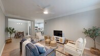 Located at 1030 Jack Primus Rd in Charleston, SC, this well-appointed 2-bedroom, 2-bathroom single-story home offers a thoughtfully designed open-concept layout. Light wood-look flooring flows throughout the main living areas, complemented by crown molding and a neutral gray-toned palette that creates a bright, cohesive ambiance.

The living room features a ceiling fan, a built-in desk nook, and connects seamlessly to the dining area and kitchen. The dining room is anchored by an elegant chandelier and is accented with coastal-inspired wall art, lending a relaxed Lowcountry feel. The kitchen is a standout, boasting white shaker cabinetry, a subway tile backsplash, stone-look quartz countertops extending to a breakfast bar, and stainless steel appliances.

The spacious primary bedroom offers generous closet space and plush carpeting, while the second bedroom benefits from abundant natural light through multiple windows. Both bathrooms are finished with white cabinetry, quartz countertops, and clean, modern fixtures — one featuring a full tub-shower combo. A dedicated laundry room houses a full-size washer and dryer. Crown molding and consistent finishes throughout reflect careful attention to detail in every room.
