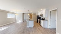 This single-floor residence offers a thoughtfully designed layout that balances open living spaces with comfortable private areas. The heart of the home is an open-concept kitchen and living area finished with light wood-look flooring throughout. The kitchen is equipped with white shaker cabinetry, granite countertops, stainless steel appliances including a gas range, microwave, and refrigerator, and a large island with pendant lighting overhead — ideal for both meal preparation and casual dining. The living area is generously proportioned, bathed in natural light from multiple large windows dressed with vertical blinds. The bedrooms feature plush carpeting, neutral-toned walls, and ample natural light, creating a calm and restful atmosphere. A spacious walk-in closet with wire shelving provides substantial storage. The two bathrooms are finished with large-format gray tile flooring and matching tiled walls. One bathroom features a sleek sliding-glass walk-in shower, while the other offers a full soaking tub with a tiled surround. Both bathrooms include white vanities with granite countertops and brushed nickel fixtures. The consistent use of neutral tones and modern finishes throughout gives the space a clean, cohesive, and move-in ready appeal.