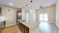 This single-floor residence presents a clean, modern aesthetic throughout, characterized by light neutral tones, hardwood-style flooring, and white panel doors that lend a cohesive, contemporary feel to every room.

The open-concept kitchen is a standout feature, anchored by a large granite-topped island with a stainless steel double sink and seating overhang. Dark espresso cabinetry provides strong visual contrast against the light surroundings, while pendant lights hang above the island for focused task lighting. Stainless steel appliances, including a refrigerator, microwave, and range, complete the well-appointed kitchen.

The living area flows naturally from the kitchen and is bathed in natural light through a set of French doors that open to an exterior view. A ceiling fan with recessed lighting overhead adds both function and comfort to the space. Notably tall ceilings in this area enhance the sense of openness.

The bedrooms are comfortably sized, each featuring hardwood-style flooring, ceiling fans, and windows fitted with blinds for privacy. The bathroom includes a granite-topped double vanity with dark cabinetry, a soaking tub surrounded by classic white subway tile, and direct access to a walk-in closet, combining practicality with refined finishes throughout.