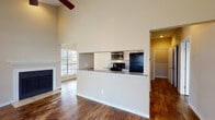 Located at 9727 Whitehurst Dr in Dallas, Texas, this single-floor residence offers a well-designed layout with a range of notable architectural features throughout. Rich, dark hardwood-style flooring runs consistently across the main living areas, complementing the warm, neutral wall tones that give the space a welcoming ambiance.

The living room is an immediate standout, boasting soaring vaulted ceilings with a ceiling fan overhead and a classic white-mantled fireplace as the focal point. Multiple windows flood the room with natural light, while a sliding glass door opens to an outdoor balcony area with views of surrounding greenery.

The galley-style kitchen is efficiently arranged with white cabinetry, granite-style countertops, and black appliances including an electric range, refrigerator, and dishwasher, along with a stainless steel microwave. A half-wall pass-through connects the kitchen to the living area, enhancing the open-concept feel.

The bedroom is generously sized, featuring its own ceiling fan, a walk-in closet, and French doors that lead to a private balcony overlooking autumn foliage. The bathroom includes a full tub-shower combination with floor-to-ceiling neutral tile surround. A dedicated entryway corridor provides a clean transition into the home's main living spaces.
