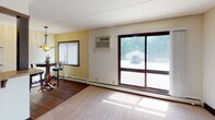 Located at 3535 Bryant Ave S in Minneapolis, Minnesota, this single-floor unit offers a practical and comfortable layout designed for everyday living. The kitchen is equipped with dark espresso cabinetry, granite-style countertops, hardwood flooring, and a full suite of stainless steel appliances including a gas range, over-the-range microwave, and a full-size refrigerator, providing a well-organized space for cooking and meal preparation. Adjacent to the kitchen, a cozy dining nook features warm hardwood floors, soft yellow walls, and a pendant light fixture overhead, with a window fitted with vertical blinds that allows natural light to filter in. The spacious living area is finished with plush carpeting, dark wood baseboards, and a large sliding glass door that opens to an outdoor view, filling the room with abundant natural light. A wall-mounted air conditioning unit ensures year-round comfort. The bedroom offers carpeted floors, a ceiling fan with a light fixture, a baseboard heating unit, and a window with vertical blinds that brings in natural light. Throughout the unit, textured ceilings, dark wood window trim, and baseboard heating create a cohesive and practical aesthetic suited to Minneapolis living.