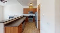 Located at 6914 Pacific Ave SE in Lacey, Washington, this single-floor home offers a clean, functional layout with a welcoming atmosphere. The living area is generously sized, featuring plush carpeting, warm wood baseboards and trim, and a ceiling fan overhead. Large windows and a glass-paneled exterior door flood the space with natural light and provide views of the surrounding neighborhood, creating an airy, open feel.

The kitchen is well-appointed with warm wood cabinetry that extends to the upper walls for ample storage, dark countertops, a double basin sink, and a full suite of stainless steel appliances including a refrigerator, electric range, microwave, and dishwasher. Tile flooring adds a practical and durable touch to this functional cooking space.

The bedrooms are carpeted and feature wood-toned bi-fold closet doors, providing a cohesive design language that runs throughout the home. A hallway landing with a warm-toned wood door and soft wall sconce lighting connects the spaces seamlessly, contributing to the home's tidy and consistent interior style. Overall, the space presents a practical and comfortable living environment with thoughtful design details and a neutral palette ready for personalization.
