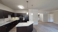 This single-floor, 2-bedroom, 2-bathroom residence offers a thoughtfully designed open layout that connects the living, dining, and kitchen areas seamlessly. The kitchen serves as a functional centerpiece, featuring dark espresso cabinetry, granite-style countertops, a peninsula island with pendant lighting overhead, and a full suite of black appliances including a range, microwave, dishwasher, and refrigerator. Wood-style flooring grounds the kitchen area, while plush carpeting extends through the living room and bedrooms.

The spacious living area is accented with crown molding and benefits from large sliding glass doors fitted with vertical blinds, allowing ample natural light and outdoor views. Both bedrooms are generously sized, each equipped with a ceiling fan, large windows, and plush carpeting. The primary bedroom features multiple closet doors, offering notable storage capacity.

A dedicated in-unit laundry area with a washer is conveniently accessible from the living space. Crown molding details in the main living area add an elegant finishing touch. The overall ambiance is clean, neutral, and move-in ready, combining practical functionality with comfortable, contemporary design.