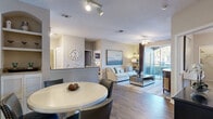Located in East Lake, FL, this thoughtfully designed 2-bedroom, 2-bathroom residence offers a comfortable and functional single-floor layout. The open-concept living and dining area is anchored by wood-look flooring, a ceiling fan, and a sliding glass door that opens onto a private balcony, allowing natural light to flow freely throughout the space. The adjoining kitchen features cream cabinetry with open shelving, a diagonal tile backsplash, light countertops, black appliances including a range and refrigerator, and tile flooring — all connected to the dining area via a convenient breakfast bar with extended counter seating.

The primary bedroom is a generously sized retreat complete with plush carpeting, a ceiling fan, a walk-in closet, and an en-suite bathroom. The second bedroom also features carpet and its own closet, providing ample storage. Both bathrooms are finished with tile flooring, vanities with light countertops, and shower/tub combinations. A dedicated utility room adds everyday practicality. The overall aesthetic throughout the home is warm and neutral, with consistent finishes that create a cohesive, inviting ambiance from room to room.