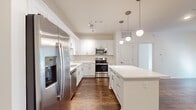 This single-story Memphis, TN residence offers a thoughtfully designed layout encompassing two bedrooms, two bathrooms, a combined kitchen and living area, and a hallway. The kitchen serves as a standout feature, showcasing white shaker cabinetry, quartz countertops, a center island with pendant lighting overhead, and a full suite of stainless steel appliances including a French door refrigerator, range, microwave, and dishwasher. Rich, dark hardwood flooring runs throughout the main living areas, adding warmth and contrast to the bright, neutral color palette. The living room benefits from natural light filtering through French doors, complemented by a ceiling fan above. Both bedrooms are finished with plush carpet and feature windows with blinds that allow ample daylight. The primary bedroom is a well-proportioned retreat. The bathrooms are finished with quartz vanity tops, white shaker cabinetry, subway-tiled tub surrounds, and framed mirrors. A walk-in closet with built-in shelving provides practical storage. Overall, the space maintains a clean, modern aesthetic with consistent finishes throughout.