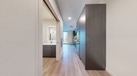 Located at 21 Boston St in Seattle, WA, this efficiently designed studio offers a thoughtfully organized single-floor layout that maximizes every square foot. Light wood-tone flooring flows throughout, tying together the open living area, kitchen, and entryway with a clean, cohesive aesthetic.

The kitchen is a standout feature, outfitted with dark-toned cabinetry accented by lighter upper cabinets, white subway tile backsplash, under-cabinet lighting, and a full suite of black stainless steel appliances including a refrigerator, dishwasher, and over-range microwave. White quartz countertops provide a crisp contrast to the rich cabinetry tones.

The bathroom is sleek and modern, featuring a dark vanity with a white countertop, an illuminated mirror, black matte hardware accents, and a glass-enclosed walk-in shower with white tile surround. A stacked washer and dryer unit is conveniently integrated within the bathroom space.

The living area benefits from a large picture window that invites abundant natural light and frames views of a landscaped courtyard below. White walls and recessed lighting keep the space feeling bright and open. The entrance provides a clean transition into the unit, completing this well-appointed, contemporary urban residence.