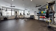 Located on W Huntingdon Street in Savannah, Georgia, this single-story fitness center is designed to support a comprehensive workout experience. The space features durable rubber flooring throughout, providing a safe and resilient surface ideal for a wide range of exercises. Recessed lighting and dual ceiling fans maintain a comfortable, well-lit environment, while multiple windows allow natural light to filter in, offering views of the surrounding greenery.

The cardio zone is equipped with Matrix treadmills, elliptical trainers, and a cable machine, all positioned near the windows to take advantage of natural light. A dedicated strength training area includes a full dumbbell rack, kettlebells, medicine balls in various weights and sizes, and a multi-functional cable and suspension training rig complete with TRX straps and a speed bag. Wall-mounted mirrors expand the visual space and assist with form monitoring during workouts.

Additional amenities include a wall-mounted flat-screen television, a built-in dual water fountain station, a towel rack, and clearly posted workout reference charts. Glass-panel doors provide easy access, and the overall layout offers ample open floor space for stretching and functional movement exercises.