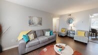 Located at 300 Pat Mell Rd in Marietta, GA, this two-bedroom, one-bathroom unit offers a well-organized single-floor layout designed for comfortable everyday living. Dark hardwood flooring runs throughout, providing a warm and cohesive feel across all rooms.

The living room is an inviting, open space bathed in natural light from large windows dressed with teal curtains. It offers generous room for seating and entertainment, flowing naturally into a dedicated dining nook that fits a round table and chairs — ideal for casual meals.

The kitchen features white cabinetry, granite-style countertops, a gray subway tile backsplash, a double stainless steel sink, and a full-size stainless steel refrigerator, offering both functionality and a clean aesthetic.

The spacious primary bedroom includes a ceiling fan, a large window with vertical blinds and sheer orange curtains, and ample natural light. The second bedroom is versatile, currently configured as a home office with plantation shutters and a ceiling fan. A hallway connects the rooms and leads to three closets and a utility room for added storage. The bathroom is clean and bright, featuring white subway tile, a vanity with under-sink storage, and a medicine cabinet mirror.