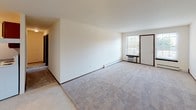 Located at 5310 Mathews Rd in Middleton, Wisconsin, this single-floor unit offers a practical and straightforward layout designed for comfortable everyday living. The floor plan reveals a spacious main living area finished with neutral wall-to-wall carpeting and crisp white walls, creating a clean, versatile backdrop. Natural light enters through multiple windows fitted with blinds, offering views of the surrounding greenery outside. Baseboard heating runs along the perimeter of the main rooms, ensuring consistent warmth throughout.

The galley-style kitchen is well-appointed with warm medium-toned wood cabinetry lining both sides, dark speckled countertops, a double-basin sink, and white appliances including an electric range and refrigerator. A ceiling fan with a light fixture is positioned at the kitchen-dining transition area, providing both ventilation and ambient lighting.

The bedrooms are carpeted and feature windows that bring in natural light along with baseboard heating. The bathroom includes light tile flooring, a towel bar, and wood-trimmed cabinetry with matching dark countertops. A wall-mounted AC unit is present in the main living area near the entry door, supplementing the climate control options. The overall ambiance is functional and understated, offering a comfortable, move-in-ready environment.