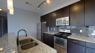 Located at 720 Michigan Ave in Columbus, Ohio, this single-floor residence offers a thoughtfully designed living space with a modern aesthetic. The kitchen stands out as a centerpiece of the home, showcasing rich, dark espresso cabinetry that extends to the ceiling for generous storage capacity. Granite countertops with subtle veining provide an elegant and durable workspace, complemented by a deep double-basin stainless steel sink. A full suite of stainless steel appliances — including a French door refrigerator, a gas range with oven, and an over-the-range microwave — caters to both everyday cooking and more elaborate culinary endeavors. A classic gray subway tile backsplash adds texture and visual interest, tying the kitchen's design elements together cohesively. Track lighting overhead ensures the workspace is well-lit and functional. The open layout of the kitchen allows for a natural flow into the surrounding living areas, creating a connected and welcoming environment. The overall ambiance of the space is clean, contemporary, and polished, making it well-suited for those who appreciate modern design paired with practical, high-quality finishes throughout.