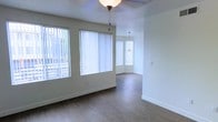 This two-floor space offers a clean, modern aesthetic defined by an open layout and an abundance of natural light. The main living area features smooth hardwood-style flooring in a warm neutral tone, complementing the crisp white walls and white baseboards that run throughout. Large windows dressed with vertical blinds line the walls, flooding the interior with daylight and creating an airy, welcoming atmosphere. A ceiling fan light fixture anchors the living space, while a stylish pendant light hangs in the adjoining area, adding a touch of character to the open floor plan. The layout flows seamlessly from one area to the next, with a bay-style windowed nook at the far end of the room providing an architectural focal point and additional light. The overall ambiance is bright, neutral, and move-in ready, with a minimalist design that allows the natural light and clean finishes to take center stage. The second floor adds valuable additional living space, making this a well-rounded, functional property suited to a variety of uses. The thoughtful combination of natural light, consistent flooring, and open sightlines gives the space a sense of openness and comfort throughout.