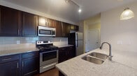 Located at 1600 W Lane Ave in Upper Arlington, Ohio, this single-floor residence offers a well-designed open-concept layout that seamlessly connects the kitchen and living areas. The kitchen is a standout feature, showcasing rich dark espresso cabinetry, light granite countertops, a classic subway tile backsplash, and a full suite of stainless steel appliances including a range, microwave, and refrigerator. A peninsula with a double stainless steel sink and pendant lighting adds both function and style, making it ideal for cooking and casual dining. The living area is generously proportioned, featuring gleaming dark hardwood floors that extend throughout the main living spaces, neutral wall tones, and a sliding glass door that opens to a balcony, inviting natural light and outdoor views. The bedroom is carpeted for comfort and features large windows that overlook the surrounding brick building exterior, providing ample natural light. A well-sized closet with built-in wire shelving offers practical storage. The bathroom is finished with large-format dark tile flooring, a granite-topped vanity with dark cabinetry, and a full tub-shower combination. Overall, the space presents a clean, modern aesthetic with consistent, quality finishes throughout.