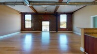 Located at 55 Green St in Clinton, MA, this thoughtfully converted mill residence masterfully combines historic industrial character with modern comfort. The open-plan living area immediately impresses with its soaring ceilings, exposed wooden beams, and industrial-style ductwork, all set above gleaming hardwood bamboo floors. Original brick walls anchor the space, while large arched and rectangular windows flood the interior with natural light and offer elevated views of the surrounding landscape.

The kitchen is well-appointed with rich warm-toned cabinetry, granite countertops, stainless steel appliances including a French-door refrigerator, electric range, and built-in microwave, all complemented by track lighting and hardwood flooring that flows seamlessly from the main living area.

The bedrooms maintain the building's signature industrial aesthetic, each featuring exposed brick accent walls, original timber beam details, tall windows with scenic outdoor views, and plush carpeting for comfort. Sturdy original wooden columns add authenticity throughout.

The bathroom offers a functional and clean layout with tile flooring, a full tub/shower combination, granite vanity, and accessibility grab bars. A stacked in-unit washer and dryer provide added convenience. The space as a whole offers a compelling fusion of historic mill architecture and contemporary residential living.