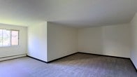 Located at 4920–4950 City Apartments in Philadelphia, PA 19131, this single-floor residence offers a straightforward and functional layout designed for comfortable everyday living. The interior presents a clean, neutral aesthetic throughout, with smooth white walls and dark baseboards that create a crisp, defined contrast along the floor line. The living area is carpeted in a light neutral tone, lending a soft, warm feel underfoot while contributing to the overall understated character of the space. The open corner design of the main living area allows for flexible furniture arrangement, making it easy to personalize the layout to suit individual needs. Ceilings are standard height and finished in white, keeping the space feeling bright and airy. The unit's simple, uncluttered design provides a blank canvas ideal for a range of furnishing styles. As part of the City Apartments community, residents benefit from an established Philadelphia neighborhood setting. The space is well-suited for those seeking a practical, no-frills residence with the convenience of city living in the 19131 zip code area of West Philadelphia.