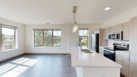 This thoughtfully designed single-floor residence offers a clean, contemporary aesthetic characterized by crisp white walls, warm wood-tone flooring, and an abundance of natural light throughout. The open-concept kitchen and living area serves as the heart of the home, anchored by a spacious island with a white quartz countertop, an undermount double sink, and stylish pendant lighting. The kitchen features light wood cabinetry, a classic white subway tile backsplash, and a full suite of stainless steel appliances, including a bottom-freezer refrigerator, electric range, and built-in microwave. Large windows in the living area frame views of the surrounding neighborhood and greenery, filling the space with natural light. The bedrooms are generously sized, each benefiting from large windows that continue the theme of brightness and openness, with ample wall space and hardwood-style flooring. Two bathrooms serve the residence: one features a walk-in glass-door shower with a light wood vanity and quartz countertop, while the second offers a full soaking tub and shower combination, also finished with a quartz-topped vanity and brushed nickel fixtures. The overall ambiance is fresh, modern, and move-in ready.