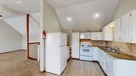 This two-story home offers six bedrooms and two full bathrooms distributed across two floors, making it well-suited for large households or shared occupancy. The ground floor provides the more spacious of the two levels, while the upper floor offers a slightly more compact layout.

The kitchen is a functional and visually appealing space, featuring white cabinetry, a stone-tile backsplash, granite-style countertops, a double sink, and white appliances including a refrigerator, electric range, microwave, and dishwasher. Light wood-style flooring runs throughout the kitchen, and the vaulted ceiling adds an open, airy feel to the space.

Adjacent to the kitchen, a large carpeted living area features multiple windows that allow generous natural light, along with a ceiling fan overhead. The vaulted ceiling continues here, enhancing the sense of openness.

The bedrooms are carpeted and vary in size, with the primary bedroom featuring vaulted ceilings and a window. Closets with built-in hanging rods provide practical storage. The two bathrooms each include a vanity with a wide mirror and warm wood cabinetry. A carpeted staircase with a wood-trimmed railing connects the floors, flanked by a hallway with light wood flooring and textured walls.