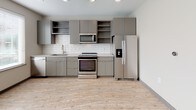 Located at 1005 W Main St in Durham, NC, this single-floor unit delivers a clean, modern aesthetic with thoughtful design details throughout. Light wood-look flooring runs continuously across the space, complemented by neutral warm-gray walls and dark baseboards that frame each room with subtle contrast.

The kitchen is a standout feature, outfitted with flat-front gray cabinetry, open upper shelving, and a classic white subway tile backsplash. A full suite of stainless steel appliances — including a side-by-side refrigerator, electric range, over-the-range microwave, and dishwasher — provides a functional and stylish cooking environment. Light-colored countertops and a single-basin sink complete the space, while a large window invites ample natural light.

The living area is open and flexible, offering generous space with ceiling fan, multiple electrical outlets, and a seamless visual connection to the kitchen. The layout allows for a variety of furniture arrangements to suit different needs.

The bathroom is finished with the same attention to detail, featuring a gray floating vanity with a white countertop, wood-look flooring, and a tiled walk-in shower enclosed by a glass door. Recessed lighting and clean tile work give the bathroom a contemporary, spa-like feel. Overall, the unit presents a cohesive, modern living environment.