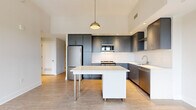 Located in the vibrant H Street corridor of Washington, DC, this three-bedroom, one-bathroom unit offers a thoughtfully designed modern interior. The open-concept kitchen and living area serves as the heart of the home, featuring sleek slate-gray cabinetry, white subway tile backsplash, stainless steel appliances, and a central island with a crisp white countertop — all beneath elevated ceilings with recessed and pendant lighting. Light wood-tone flooring flows throughout, unifying the space with a clean, contemporary aesthetic. Each of the three bedrooms is bright and airy, benefiting from large floor-to-ceiling windows with black frames that frame sweeping elevated views of the surrounding Washington, DC cityscape and tree canopy. The primary bedroom is generously proportioned and bathed in natural light through a wide bank of windows. A third bedroom features a glass-paneled interior door, adding an open, modern touch. The bathroom is clean and functional, finished with large-format white wall tiles, a soaking tub and shower combo, and brushed nickel fixtures. A dedicated closet rounds out the layout, providing practical storage. The overall ambiance is contemporary, bright, and move-in ready.