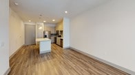 This 1-bedroom, 1-bathroom residence is thoughtfully laid out across a single floor, offering a clean and modern aesthetic throughout. The open-concept living and kitchen area is anchored by warm wood-style luxury vinyl plank flooring, recessed lighting, and a central island with a crisp white countertop that doubles as a breakfast bar. Pendant lights illuminate the island, while the adjacent kitchen features light wood cabinetry, a subtle blue-gray tile backsplash, stainless steel appliances including a French door refrigerator with ice maker, electric range, over-the-range microwave, dishwasher, and a deep stainless steel sink. The living area is bright and airy, highlighted by a ceiling fan and French doors that open to an outdoor space, inviting natural light throughout. The bedroom is carpeted for comfort, features a ceiling fan with light, and includes a window with outdoor views, creating a calm and restful retreat. The full bathroom is well-appointed with a gray wood-tone vanity, white quartz countertop, a large framed mirror, and a soaking tub and shower combination with polished chrome fixtures and tile surround. Wood-style flooring continues into the bathroom, tying the space together with a cohesive, contemporary feel.
