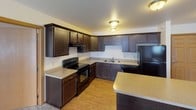 This single-floor unit offers a thoughtfully designed layout that balances comfort and functionality. The kitchen serves as a standout feature, showcasing rich dark espresso cabinetry that extends to the ceiling for generous storage, light-toned countertops, and a full suite of black appliances including a range, dishwasher, and refrigerator. Warm wood-look flooring runs throughout the kitchen and adjoining areas, complemented by flush-mount ceiling lighting that keeps the space bright and inviting. A kitchen island provides additional prep and storage space.

The bedrooms are finished with soft neutral carpet and feature baseboard heating. One bedroom includes a dedicated closet and direct access to the bathroom, lending it a private, suite-like quality. Windows allow natural light to filter in, creating an airy atmosphere throughout.

The bathroom is cleanly finished with tile flooring, a large vanity mirror, a dark wood vanity cabinet with a single sink, and a full-size tub and shower combination fitted with chrome fixtures.

A dedicated in-unit laundry room houses a full-size washer and dryer with an overhead wire shelving rack, adding practical convenience. Throughout the unit, neutral walls and warm wood trim details create a cohesive, move-in-ready aesthetic.