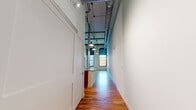 Located at 1241 College Ave SW in Lenoir, NC, this single-floor loft unit showcases a striking adaptive reuse design that preserves the raw industrial character of its origins while delivering contemporary comfort. Rich, wide-plank hardwood floors run throughout every room, lending warmth and continuity to the space. The main living area impresses with soaring ceilings, exposed ductwork, and large arched multi-pane windows that flood the room with abundant natural light and evoke the building's historic mill heritage. Original white-painted brick walls and structural columns add authenticity to the industrial aesthetic. The kitchen is well-appointed with warm wood cabinetry, granite countertops, a spacious island with a stainless steel sink, and a full suite of stainless steel appliances including a refrigerator, range, and microwave. The bedroom features impressively tall ceilings, two closets, and direct access to a private en-suite bathroom outfitted with a glass-enclosed tiled shower and a wood-vanity with a white countertop. A second bathroom provides a vanity and toilet, also finished with hardwood flooring. The overall ambiance is open, airy, and full of character — a seamless union of historic industrial design and modern living.